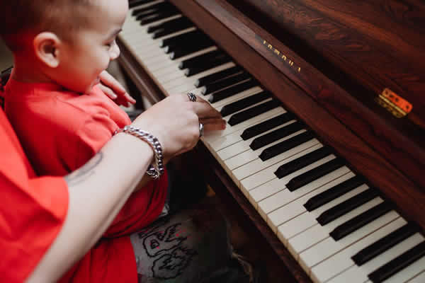 niño pequeño tocando el piano con ayuda de un adulto