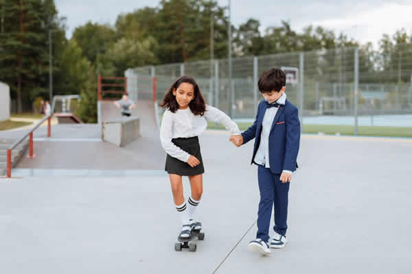 una niña aprende skate con ayuda de su amigo